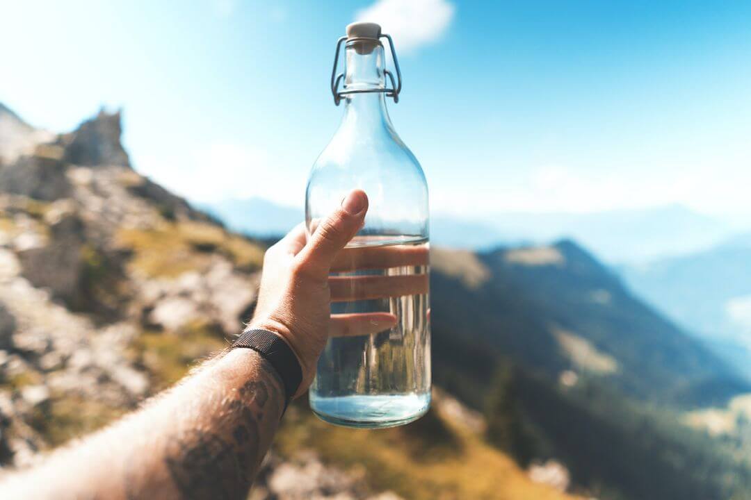 1st person view of of a person holding out a water bottle with a mountain landscape