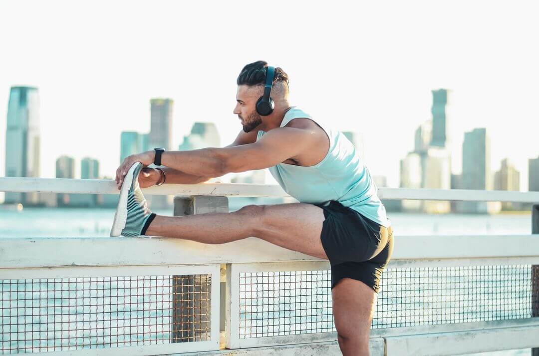 Man outdoors doing leg stretches with headphones on